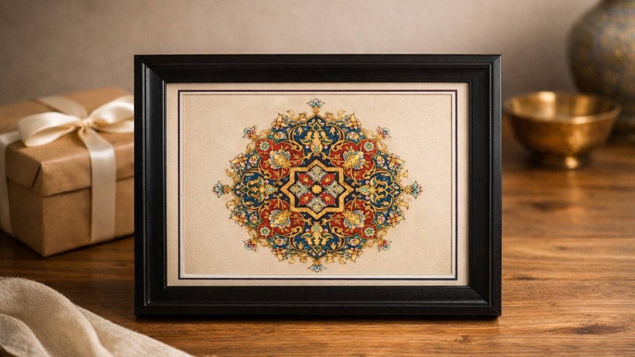 تابلوی تذهیب ایرانی قاب‌شده روی میز چوبی، اثر هنری کوچک با نقوش طلایی سنتی در سیر تحول تذهیب از نسخه های خطی تا تابلوهای مستقل